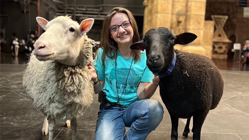 Abigail King on theatre stage smiling next to two sheep.