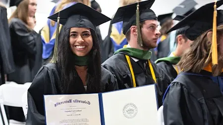 Graduate smiling with diploma at graduation ceremony.